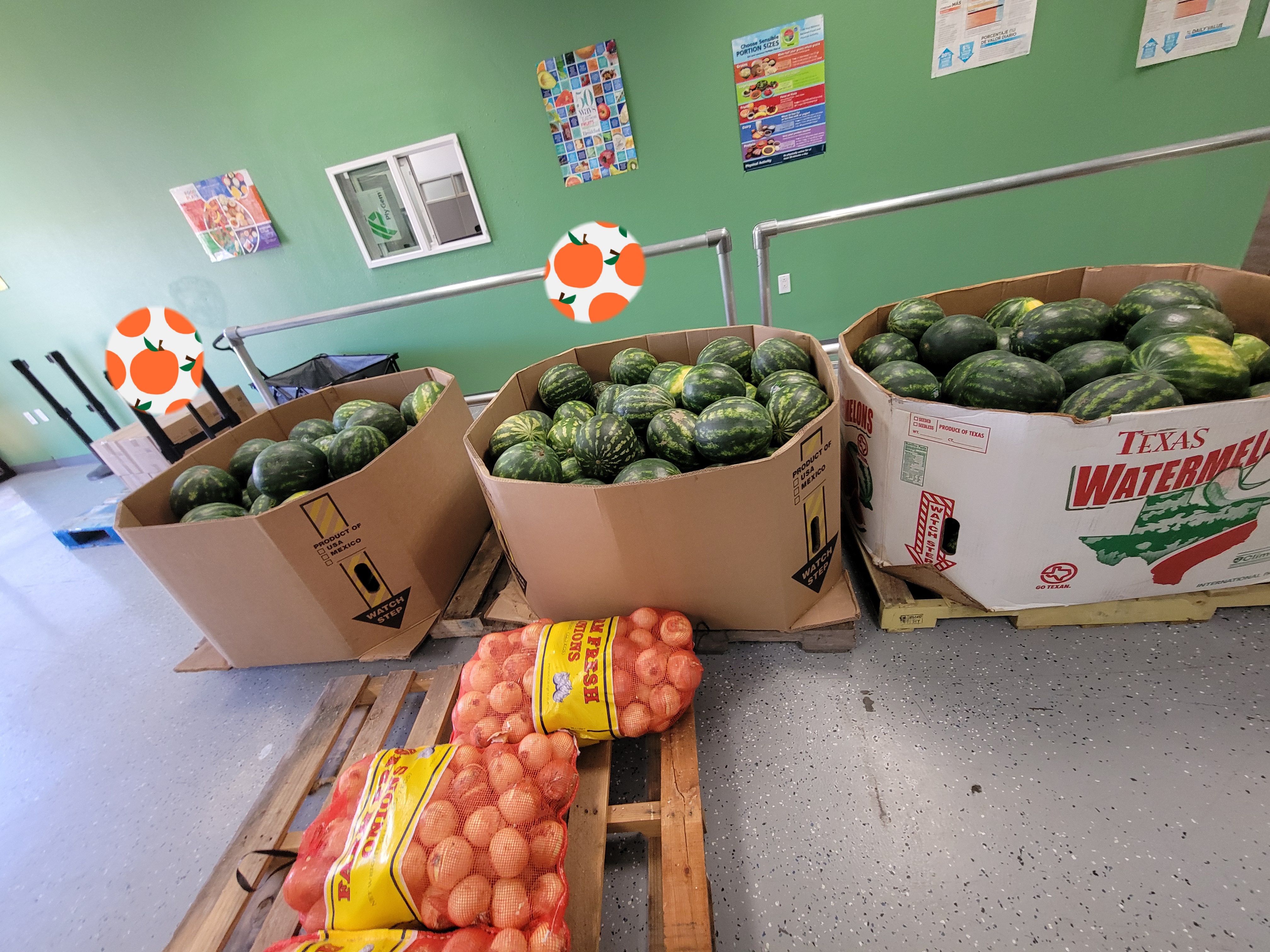 Cardboard containers filled with watermelon on pallets and another pallet with bulk bags of onions.